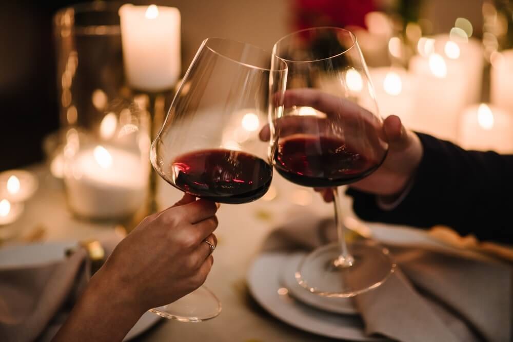 Duas taças de vinho tinto português brindando em uma mesa iluminada por velas